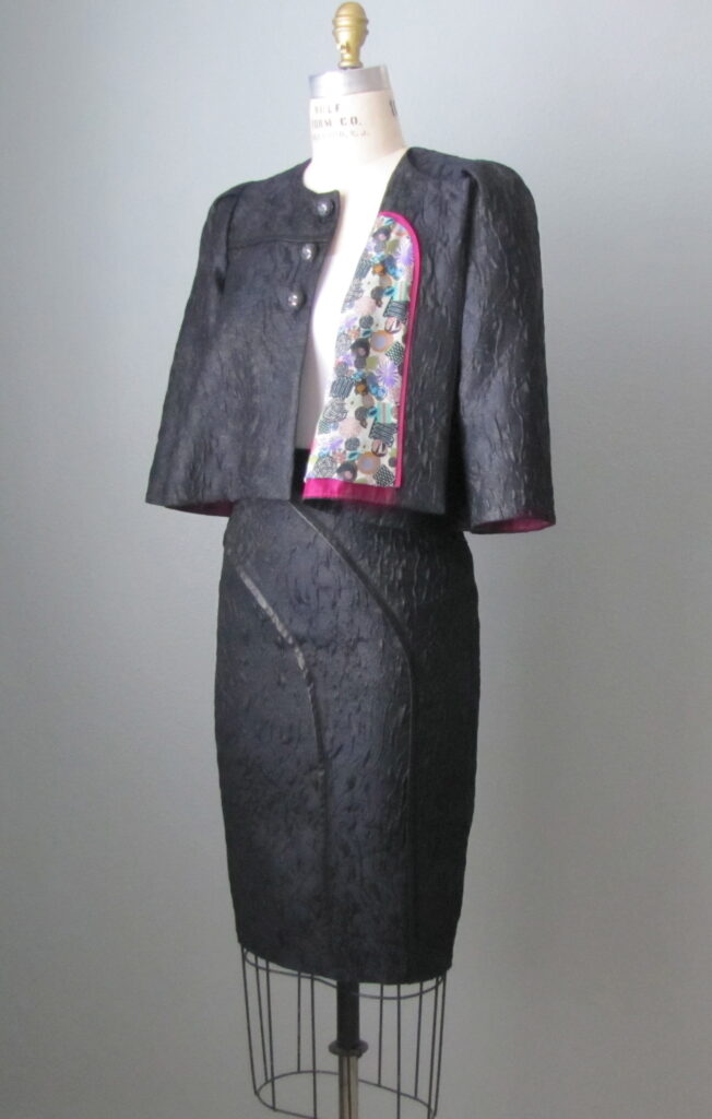 Cropped swing jacket with puff sleeves, faux leather trim, and silk lining; matching pencil skirt