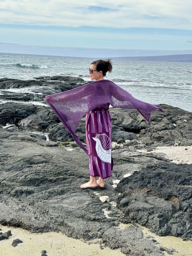 Handknit silk, cashmere, and wool wrap around shoulders at a Hawaiian beach